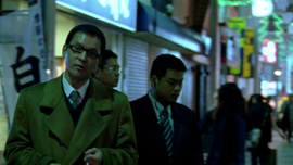 Kumagai-san and two yakuzas walk in the evening in the Tokyo’s streets. Kumagai-san and two yakuzas walk in the evening in the Tokyo’s streets.