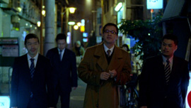 Kumagai-san and three yakuzas walk in the evening in the Tokyo’s streets. Kumagai-san and three yakuzas walk in the evening in the Tokyo’s streets.